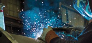 A worker welds metal wearing a bald eagle mask.