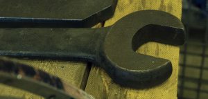 A wrench sits on a wooden work desk.