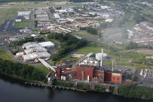 Aerial view of the NAES Hartford plant situated near a river, surrounded by industrial buildings and greenery, showcasing the facility’s scale.