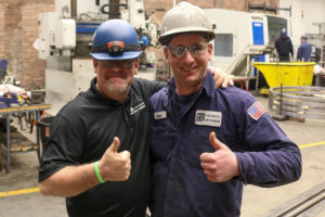 Two Helfrich Brothers employees in safety gear giving thumbs up in the workshop, showcasing teamwork and morale.