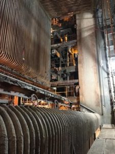 Inside view of an industrial boiler with large, curved metal tubes, showing complex piping and structural elements with a partially lit background.