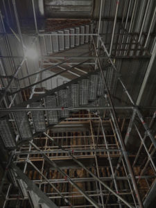A complex network of scaffolding inside an industrial facility, illuminated by overhead lighting.