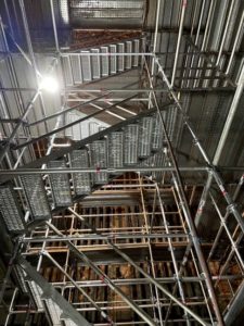 A complex network of scaffolding and metal staircases, illuminated by a bright light in an industrial setting.