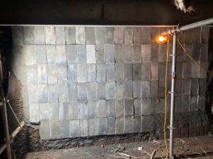 Metal panels installed on a wall, illuminated by a single work light, showing construction scaffolding.