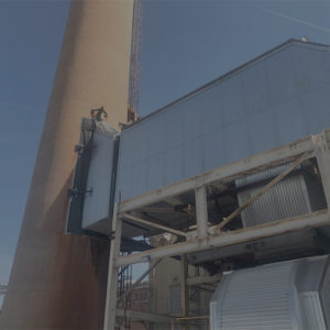 Large industrial stack with adjoining metal structures and support beams, part of a power generation facility under a clear blue sky.