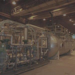 Large industrial boiler system with piping and valves in a dimly lit facility, showcasing advanced machinery for power generation.
