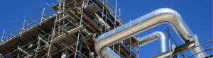 Scaffolding surrounding a large structure with shiny metal pipes curving against a bright blue sky.