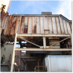 A rusted industrial structure with metal supports and various equipment, seen against a clear sky.