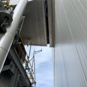 Industrial piping and scaffolding installed between two buildings with metallic cladding, viewed from below.