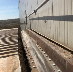 A close-up view of a bolted metal joint with protective covering, installed along the edge of a building roof under clear skies.