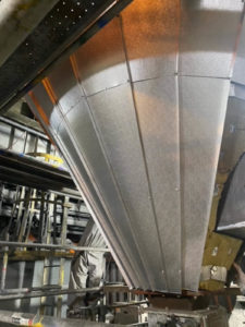 A large metal funnel-like structure being worked on in an industrial setting, with scaffolding and workers in protective suits visible.