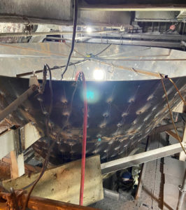 A large industrial cone structure being installed, with lights, cables, and insulation visible in the background.