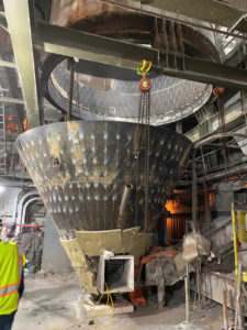 A large industrial funnel-shaped structure being serviced, supported by chains and scaffolding with insulation exposed.