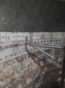A partially tiled industrial surface with hexagonal and square tiles, some of which are damaged, and metal scaffolding in place for repairs.