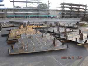 Large metal panels with attached metal rods are laid out on the ground in an industrial yard, ready for further assembly or installation.