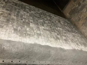A metal surface with a grid-like pattern, likely part of an industrial process, showing a rough, weathered appearance.
